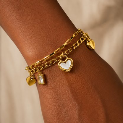 Layered gold bracelet adorned with heart charms, featuring a solid heart and a white-centered charm for elegant sophistication.