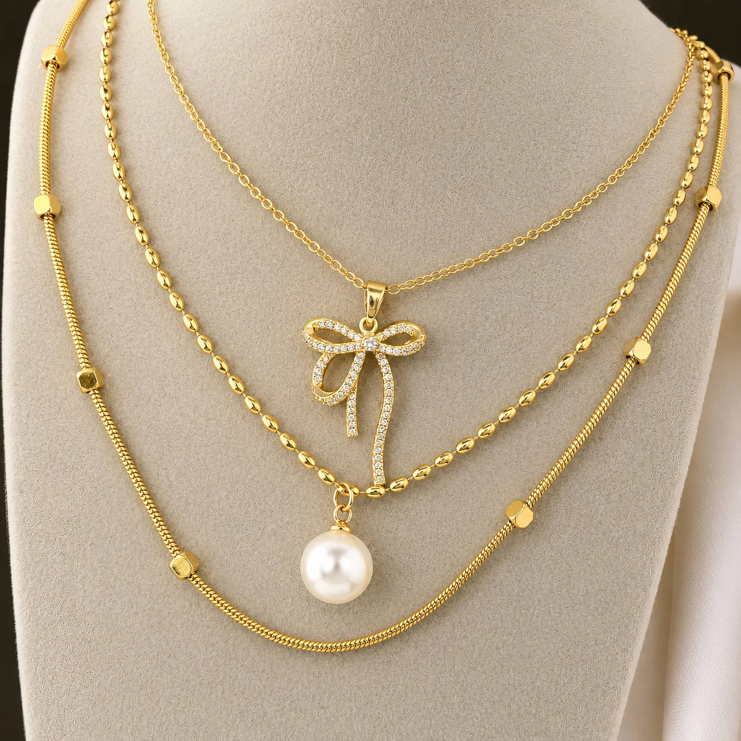 Gold necklace with bow and pearl pendant on a mannequin bust.