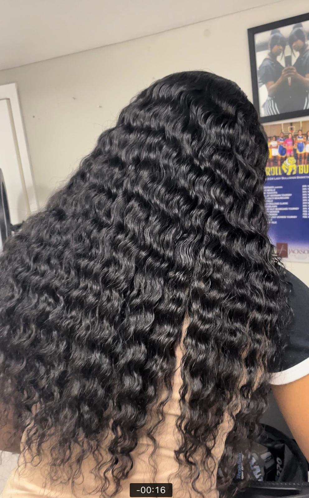 Person with long, wavy black hair sitting indoors.