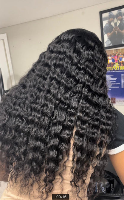 Person with long, wavy black hair sitting indoors.